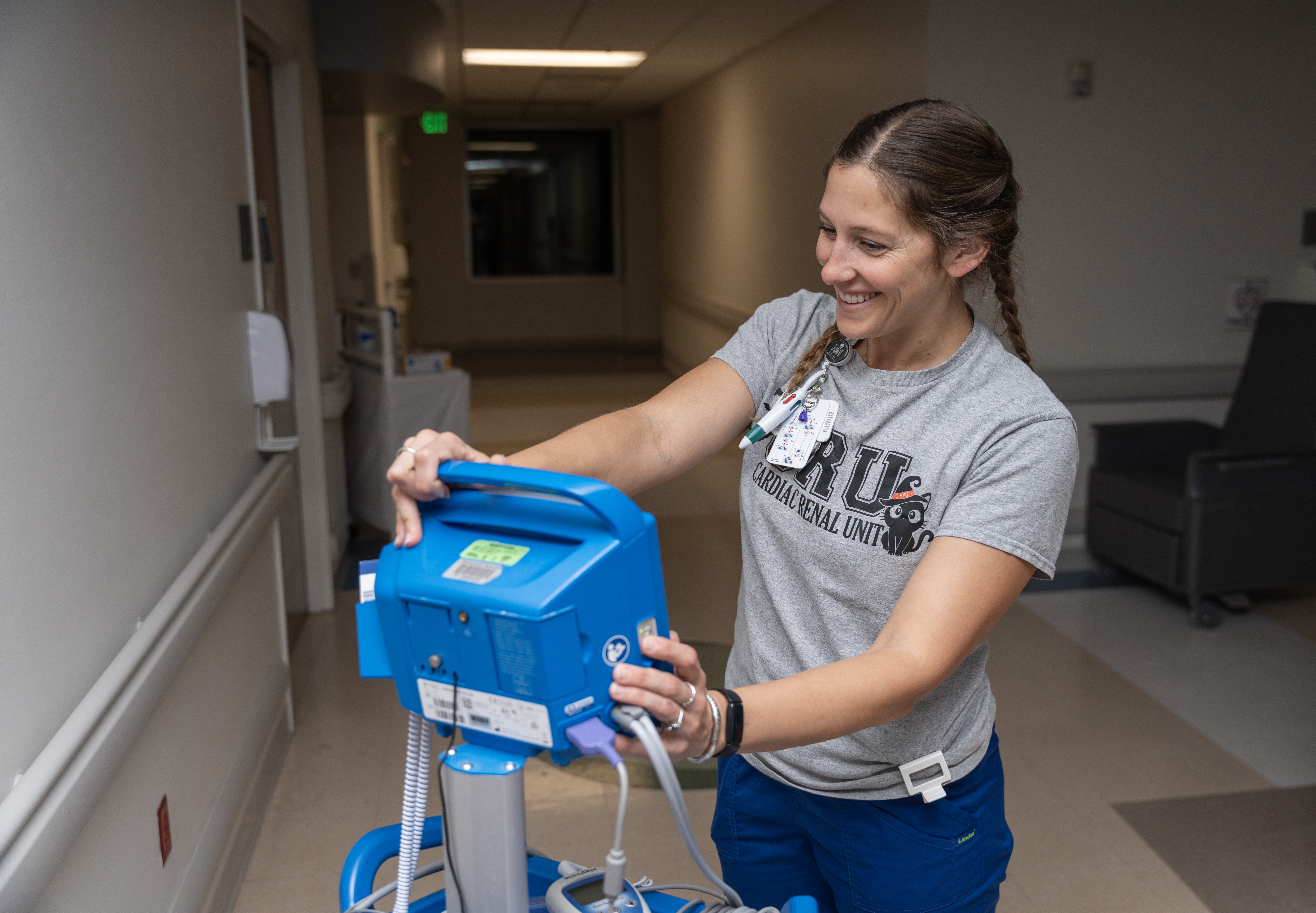smiling nursing student adjusts a blue medical device in a hospital hallway